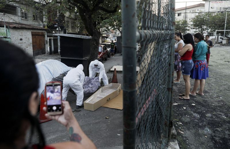 Trabajadores de una funeraria usando trajes protectores sacan el cuerpo de un hombre que murió en una calle en la comunidad de Arara tras sufrir problemas respiratorios en plena pandemia de coronavirus, en Rio de Janeiro (Reuters)