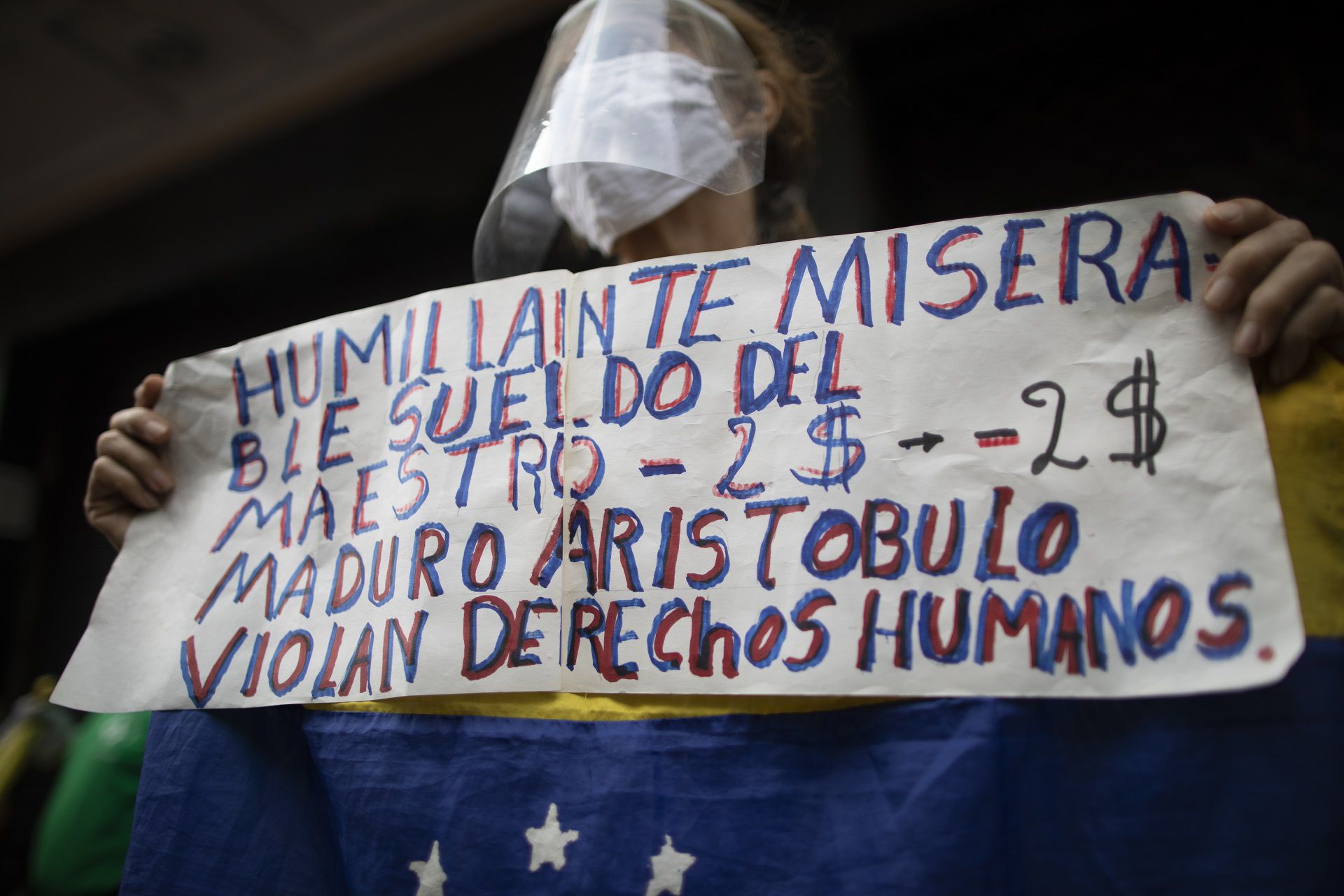 A protester holds the Spanish message: "Humiliating and miserable teachers salaries. $2 dollars," during a demonstration for higher pay in Caracas, Venezuela, Wednesday, Oct. 21, 2020. Some health workers also joined the protest and complained about their salaries of about $4 dollars a month, amid the COVID-19 pandemic. (AP Photo/Ariana Cubillos)