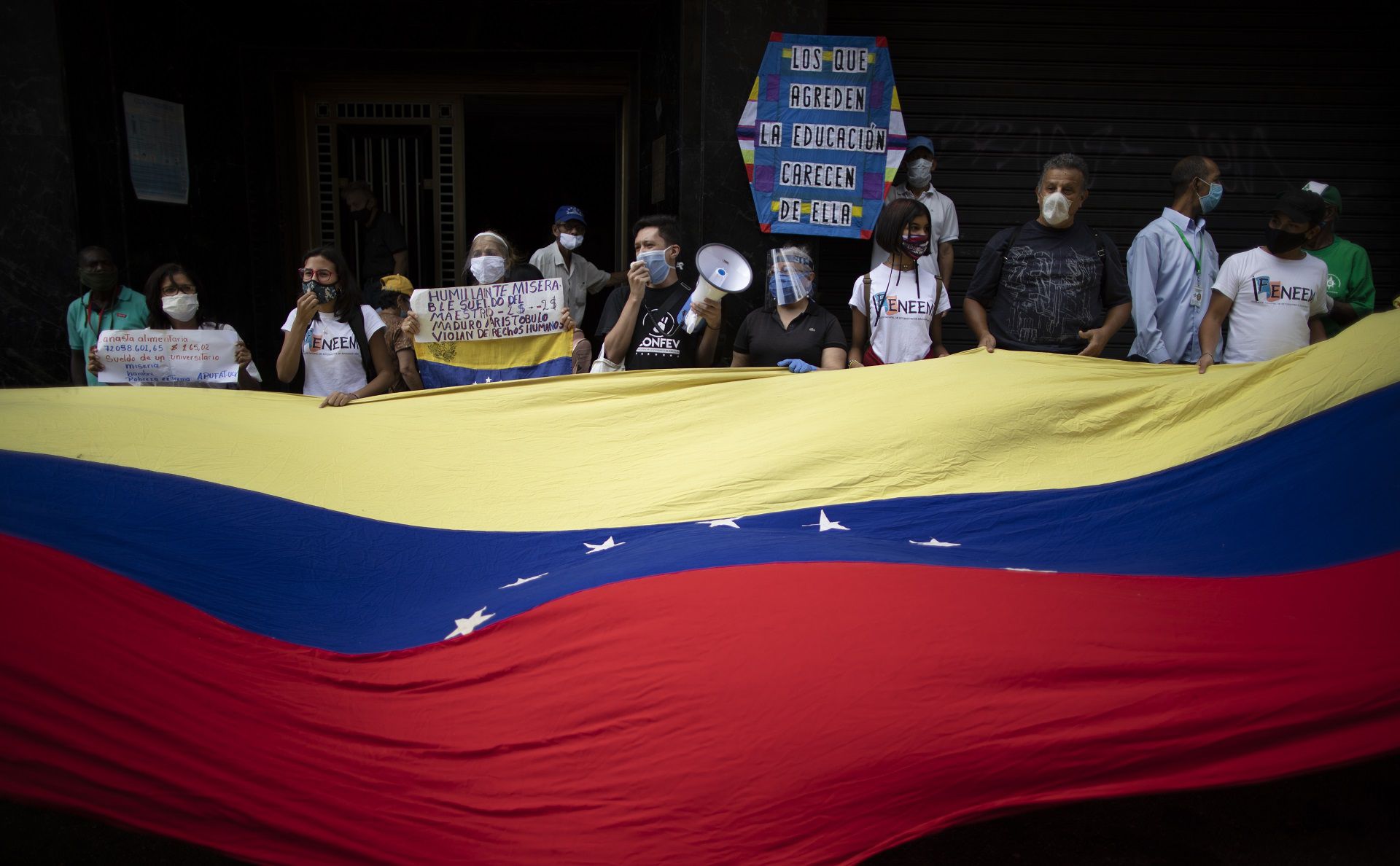 Protesters wave a Venezuelan flag during a demonstration by teachers, who make $2 dollars a month, to demand higher salaries in Caracas, Venezuela, Wednesday, Oct. 21, 2020. Amid the COVID-19 pandemic, some health workers also joined the protest and complained about their salaries of about $4 dollars a month. (AP Photo/Ariana Cubillos)