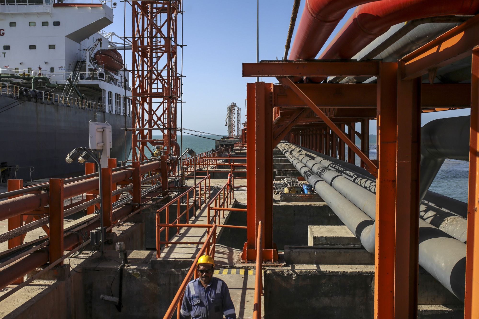 A worker walks along a jetty as a ship sits docked at the Vadinar Refinery complex operated by Nayara Energy Ltd., formerly known as Essar Oil Ltd. and now jointly owned by Rosneft Oil Co. and Trafigura Group Pte., near Vadinar, Gujarat, India, on Wednesday, April 25, 2018. The refinery was the crown jewel in a blockbuster $13 billion acquisition that, at the time, represented the largest foreign direct investment in India's history. The deal marked Trafigura's coming of age. Photographer: Dhiraj Singh/Bloomberg