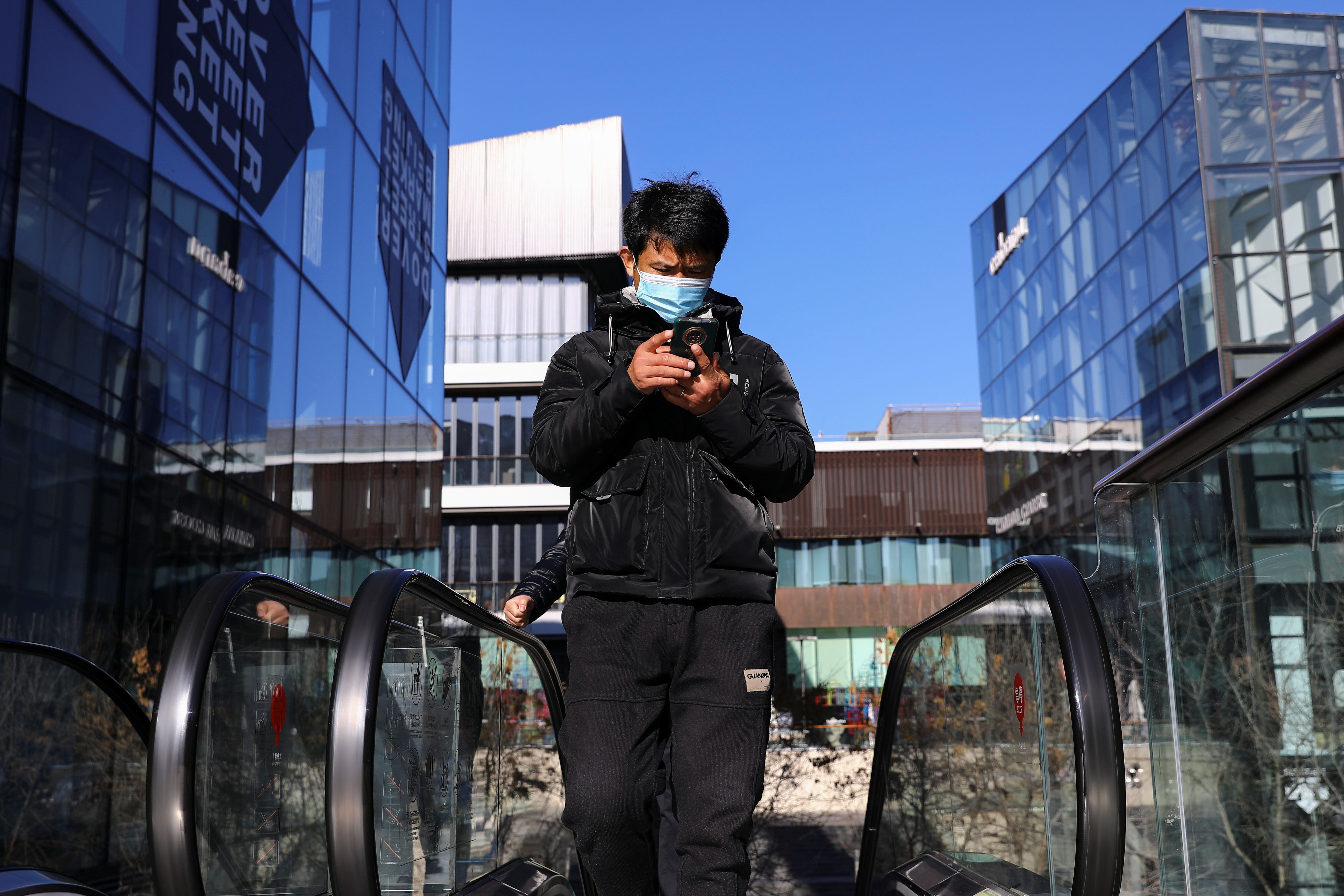 Un hombre con mascarilla para evitar la propagación de la enfermedad del coronavirus (COVID-19) revisa su teléfono mientras viaja en una escalera mecánica en un complejo comercial en Beijing, China 1 de diciembre de 2021. REUTERS/Tingshu Wang