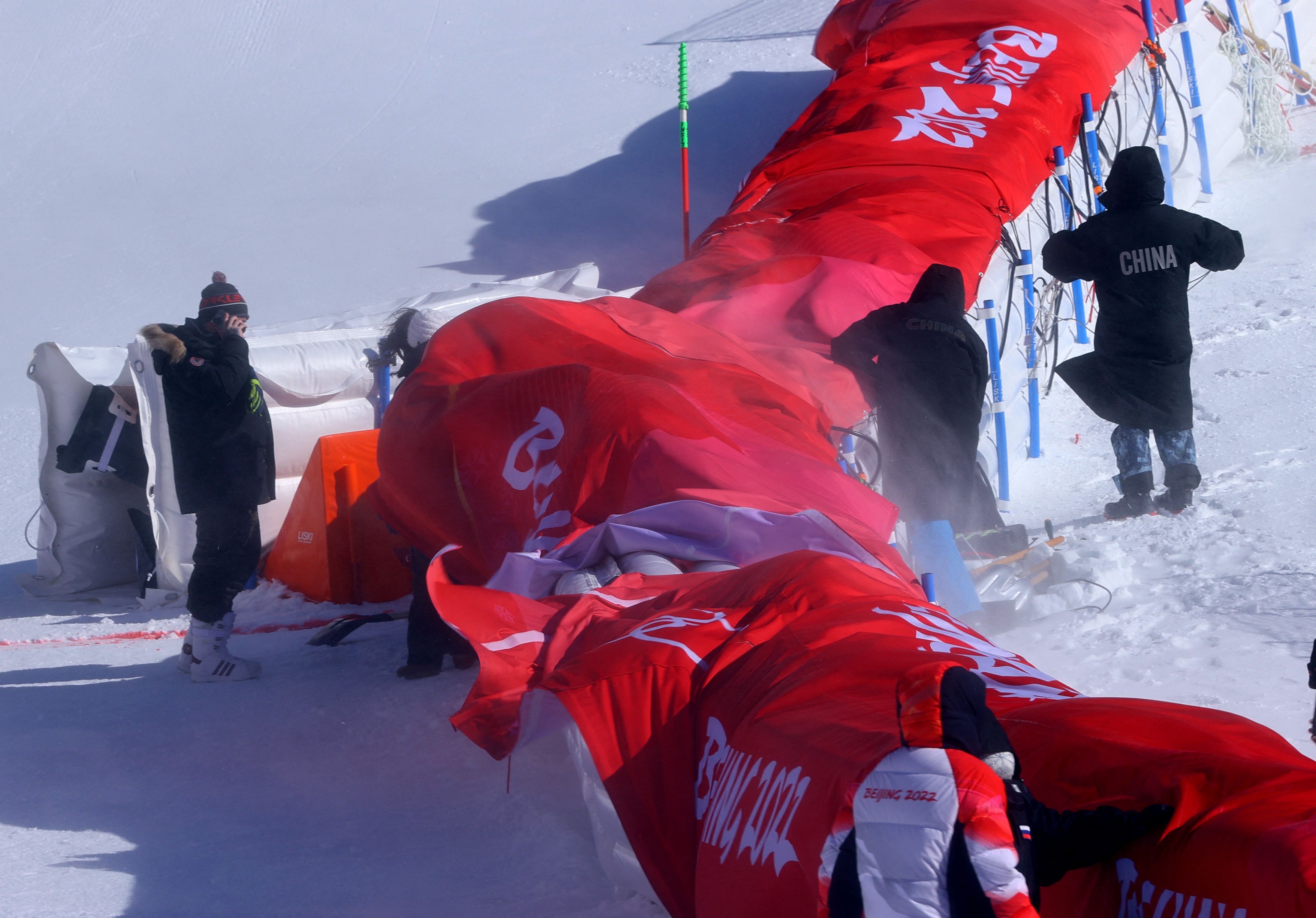 2022 Beijing Olympics - Alpine Skiing - Mixed Team Parallel 1/8 Finals - National Alpine Skiing Centre, Yanqing district, Beijing, China - February 19, 2022. People wearing ski jackets stand on the slope amidst windy conditions after organizers announced a delay to the start of the event. REUTERS/Jorge Silva