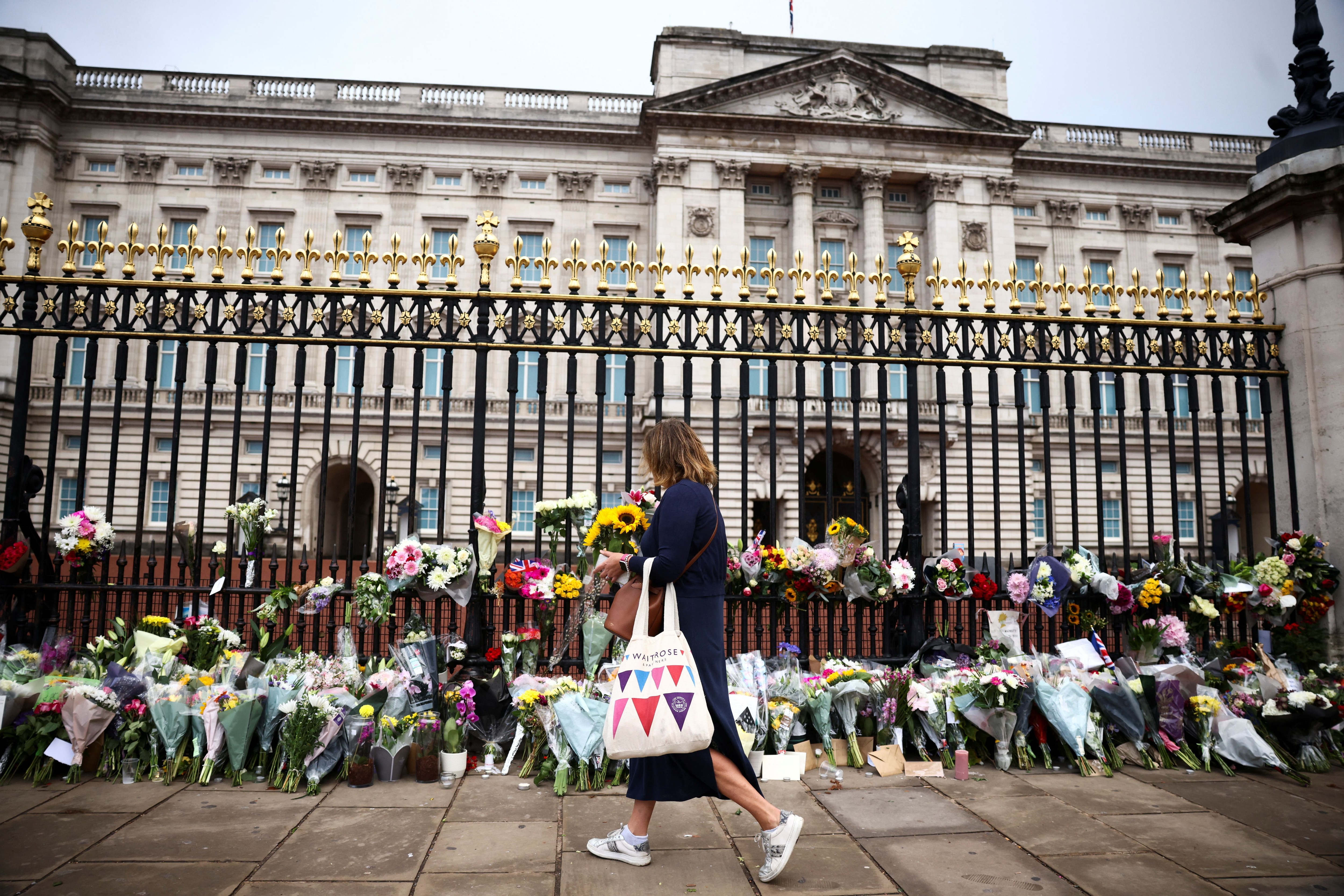 A person carries floral tribute in front of Buckingham Palace, following the passing of Queen Elizabeth, in London, Britain, September 9, 2022. REUTERS/Henry Nicholls