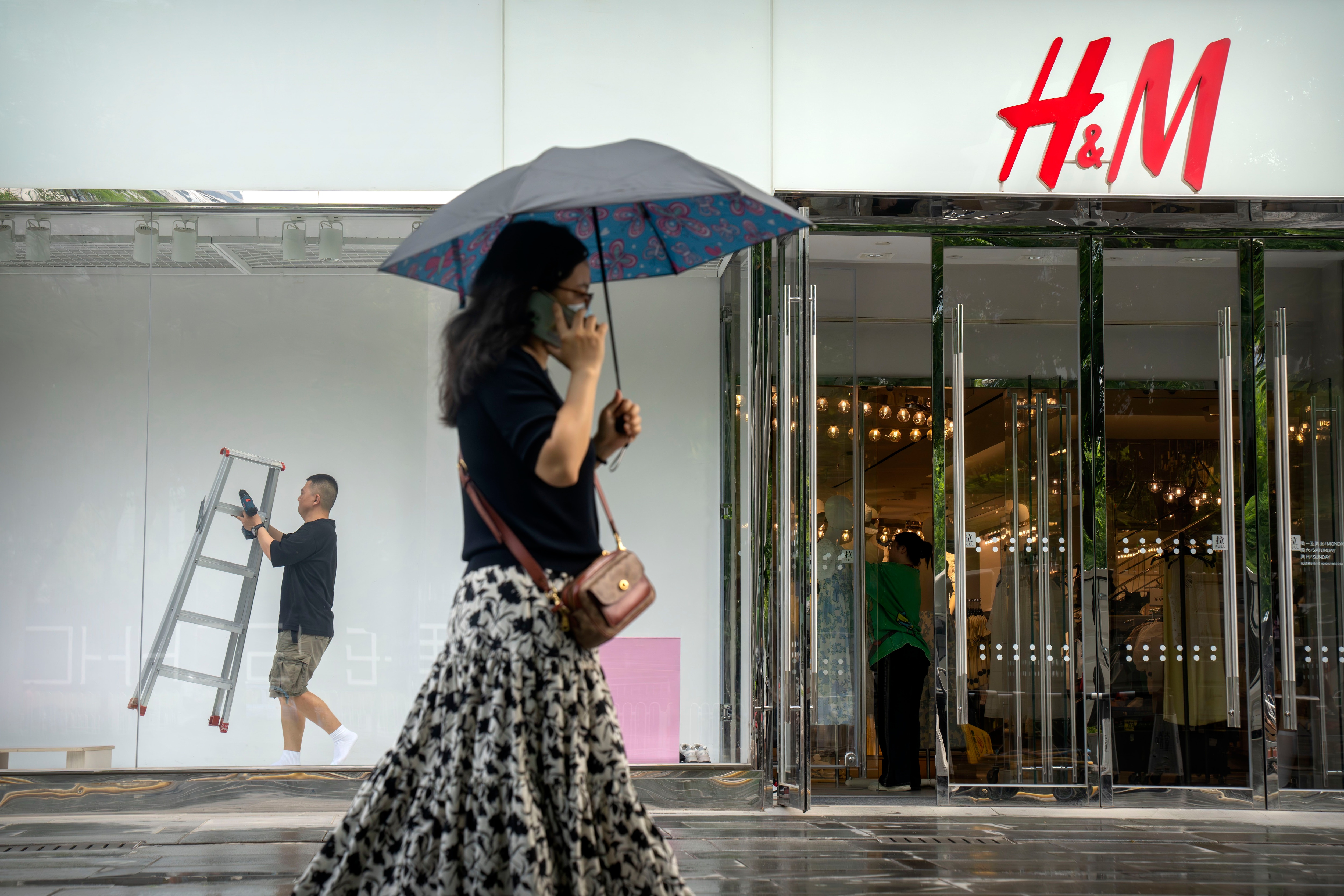 Un trabajador lleva una escalera mientras trabaja en el escaparate de una tienda de moda en Beijing, el martes 16 de mayo de 2023. La recuperación económica china se ve presionada por una débil demanda de exportaciones y consumo, según dijo el martes 16 de mayo un miembro del gobierno, después de unos datos peores de lo esperado en ventas minoristas y otros indicadores en abril. (AP Foto/Mark Schiefelbein)